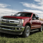 A red 2019 Ford F-250 pulls a trailer in a green field