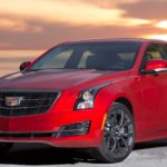 A red 2016 Cadillac ATS is parked in a road with a yellow sun set behind it.