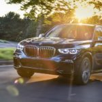 A black 2018 Used BMW X5 is driving through a parking lot with trees and sunshine.