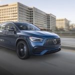 A blue 2021 Mercedes-Benz GLA SUV 250 is driving on a highway in front of a city.