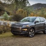 A gray 2020 Used Jeep Compass is parked on a dirt area next to a highway.