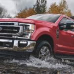 A red 2021 Ford F-250 is crossing a river.