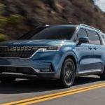 A blue 2022 Kia Carnival is shown driving from a low angle.