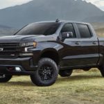 A black 2022 Chevy Silverado 1500 is shown from the side parked in a grass field in front of a stream.