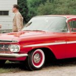 A couple is shown standing next to a red 1959 Chevy El Camino.