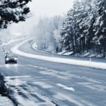 A close up shows a car driving on a snowy highway.