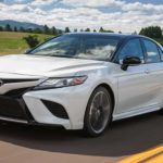 A white 2018 Toyota Camry for sale is shown driving on an open road.