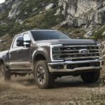 A grey 2023 Ford F-350 is shown from the front driving on a dirt road.