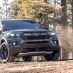 The latest Ford Explorer for sale, a dark green 2024 Ford Explorer Timberline, is shown driving in a forest.