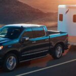 A black 2024 Chevy Silverado 1500 High Country is shown towing a trailer.