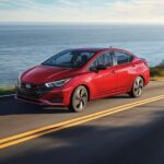 A red 2024 Nissan Versa is shown driving near an ocean.