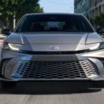 A silver 2025 Toyota Camry is shown driving on a city street.