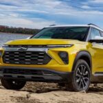 A yellow 2024 Chevy Trailblazer for sale is shown parked near an ocean.