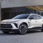 A white 2024 Chevy Blazer EV RS is shown parked outside a building after visiting a Chevy dealer.