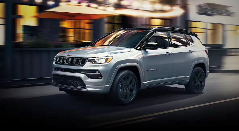 A silver 2024 Jeep Compass is shown driving to a Jeep dealership near me.