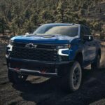 A blue 2024 Chevy Silverado 1500 for sale is shown driving off-road.