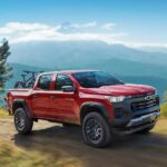 A red 2024 Chevy Colorado is shown driving off-road after visiting a Chevy dealer.