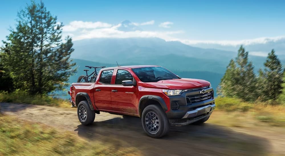 A red 2024 Chevy Colorado is shown driving off-road after visiting a Chevy dealer.