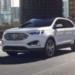 A white 2024 Ford Edge Titanium is shown driving on a bridge.