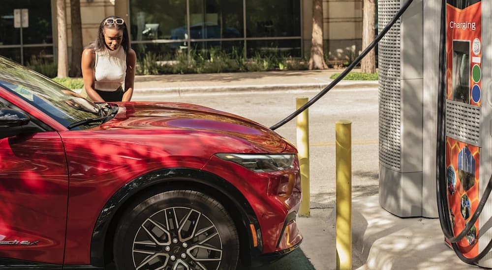 A woman is charging a red 2024 Ford Mustang Mach-E at a public charging station.