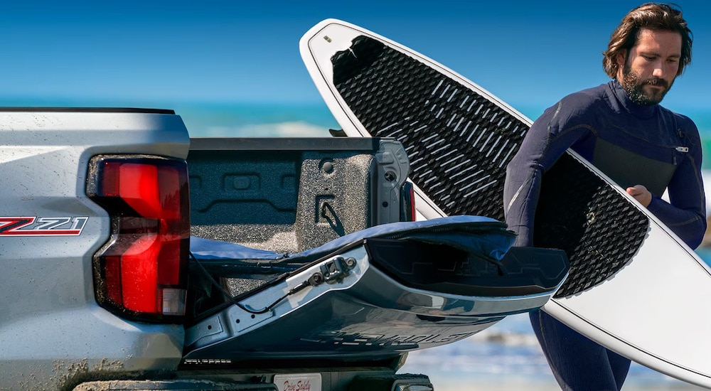 A surfer is shown unloading his board from the bed of a silver 2024 Chevy Colorado Z71.