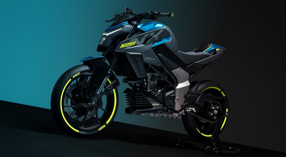 A black, blue and neon yellow CFMOTO 125NK is shown parked near a motorcycle dealer.