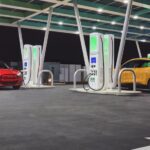 A red and a yellow 2024 Ford Mustang Mach-E parked at an EV charging station.