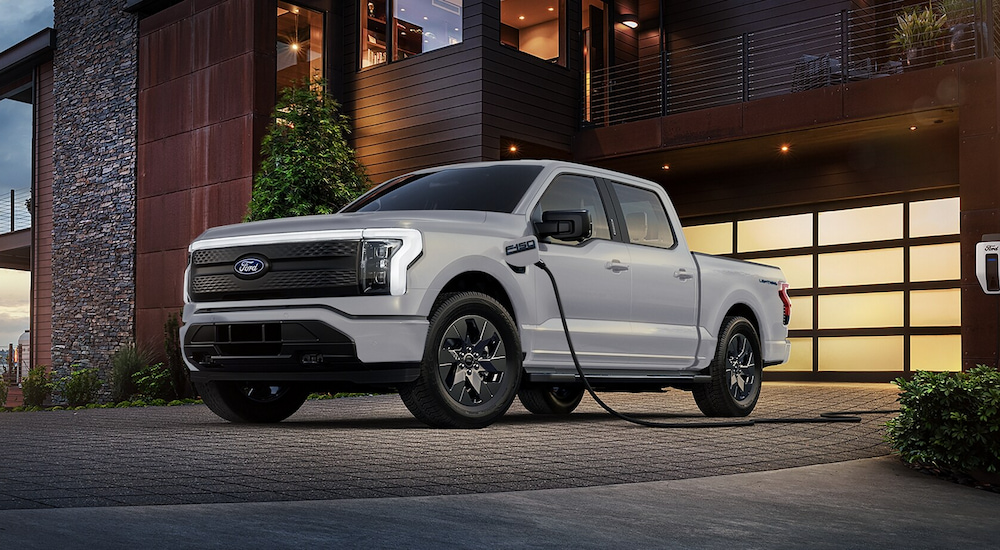 A white 2024 Ford F-150 Lightning plugged into a home charging station.