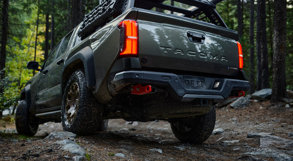 A low-angle rear view of a green 2024 Toyota Tacoma Trailhunter Hybrid driving through the woods.