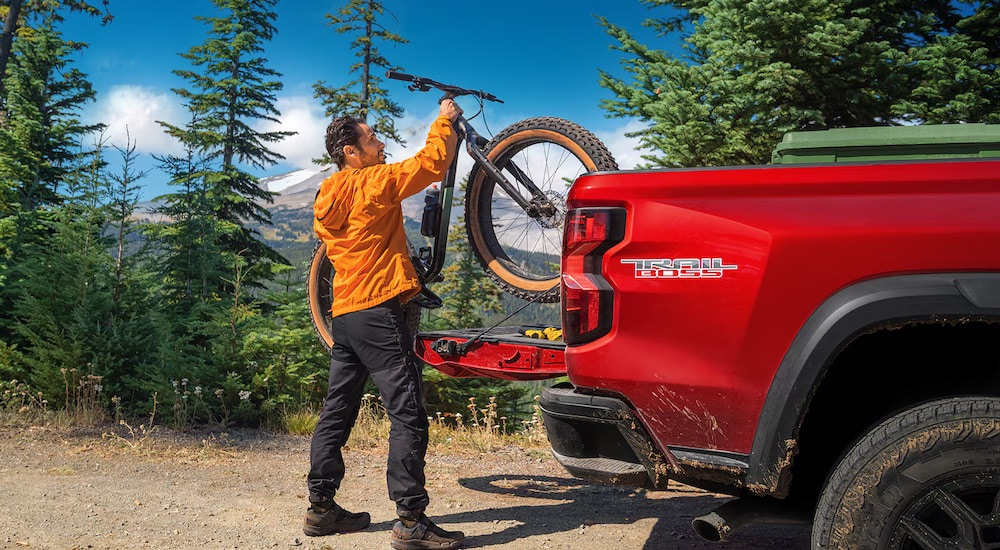 A person is shown loading a bike into the back of a red 2023 Chevy Colorado Trail Boss.