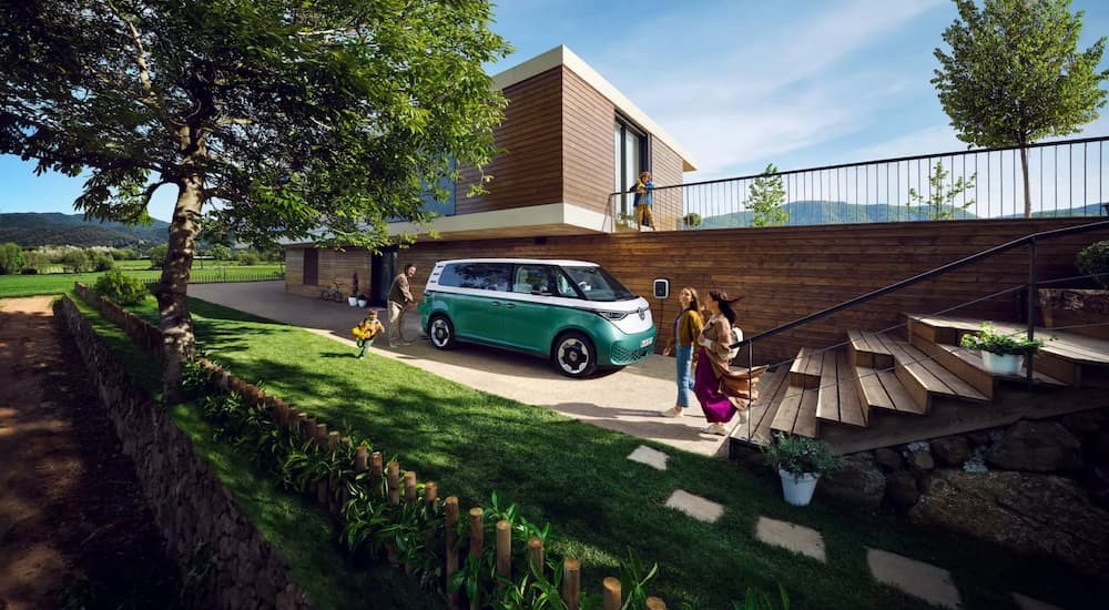 A green and white 2025 Volkswagen ID.Buzz is shown parked near a modern house.