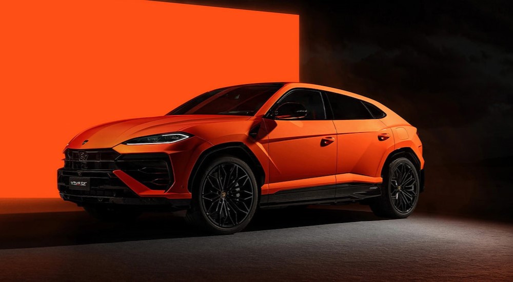 An orange 2025 Lamborghini Urus SE is shown parked in a black and orange room.