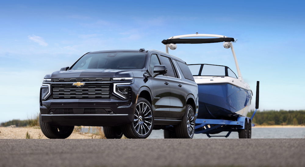 A black 2025 Chevy Suburban High Country is shown from the front while towing a boat after leaving a Chevy dealer.