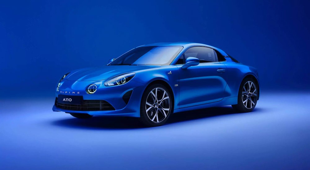 A blue 2024 Alpine A110 is shown parked in a blue showroom.