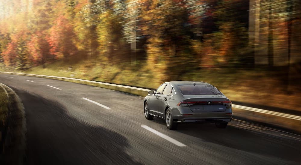 A rear view of a grey 2024 Honda Accord driving from a dealer with a Honda Accord for sale.