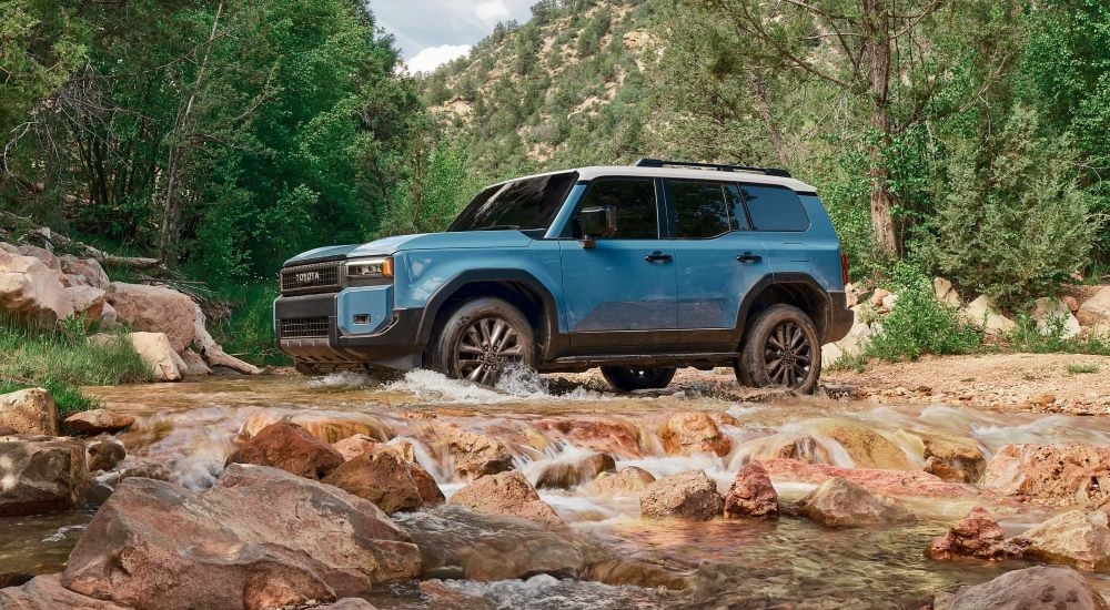 Side angle view of a blue 2024 Toyota Land Cruiser parked by a creek.