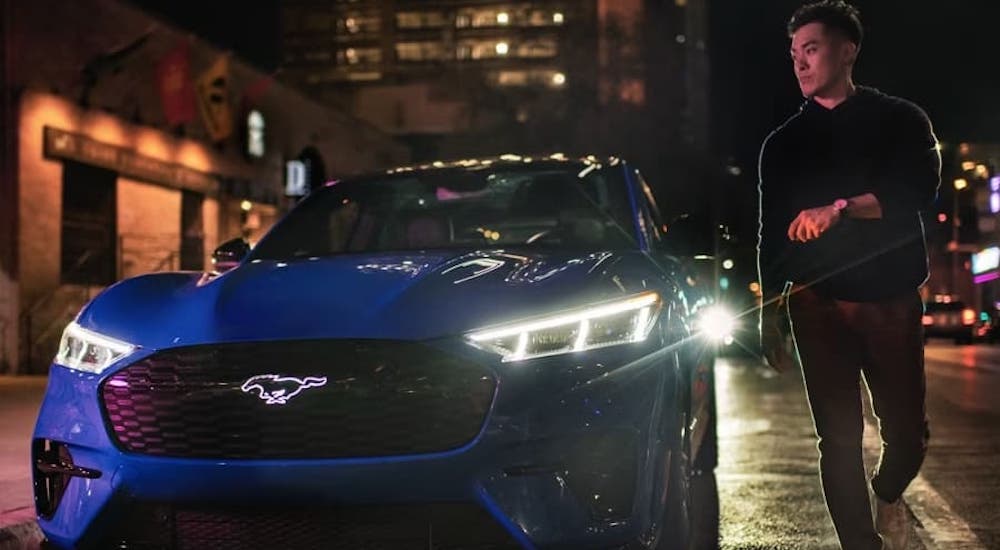 A person parking a blue 2023 Ford Mustang Mach-E GT by a curb after visiting a Ford dealer.