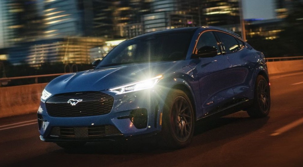 A blue 2024 Ford Mustang Mach-E driving through a city at night.