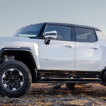 Side view of a white 2024 GMC Hummer EV Pickup parked on a mountaintop.