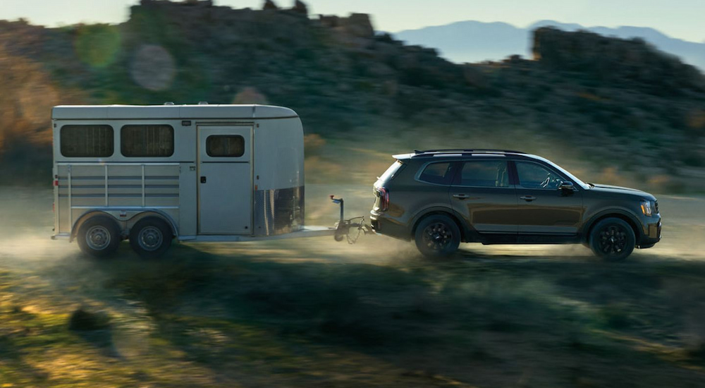 A black 2024 Kia Telluride X-Pro towing a trailer on a dusty road.