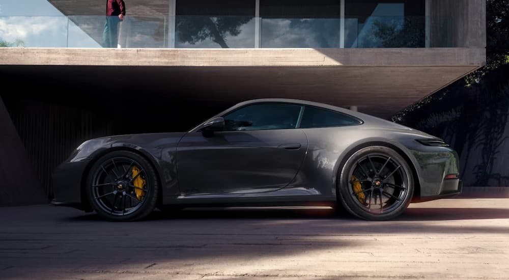 A gray 2025 Porsche 911 Carrera GTS Hybrid is shown parked near a modern building.