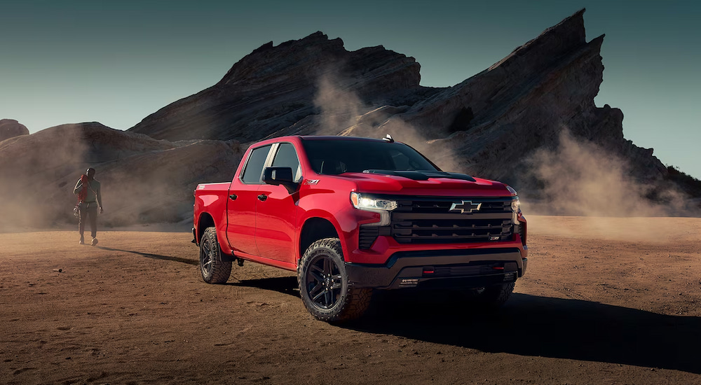 A rock climber walking towards a red 2024 Chevy Silverado 1500 LT Trail Boss parked near cliffs.