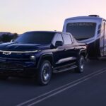 A black 2024 Chevy Silverado EV towing an RV on the highway.