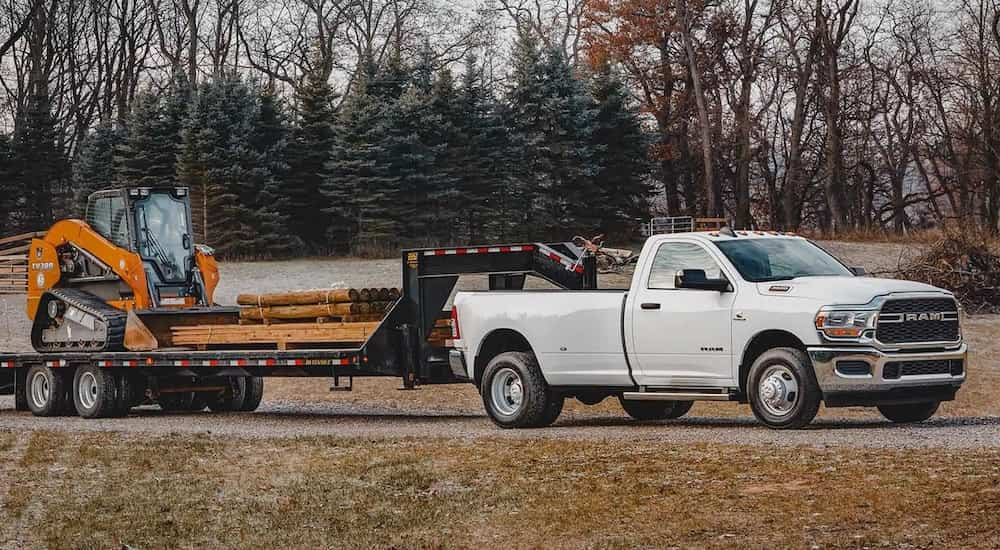 A white 2024 Ram 3500 for sale is shown from the side while towing a trailer.