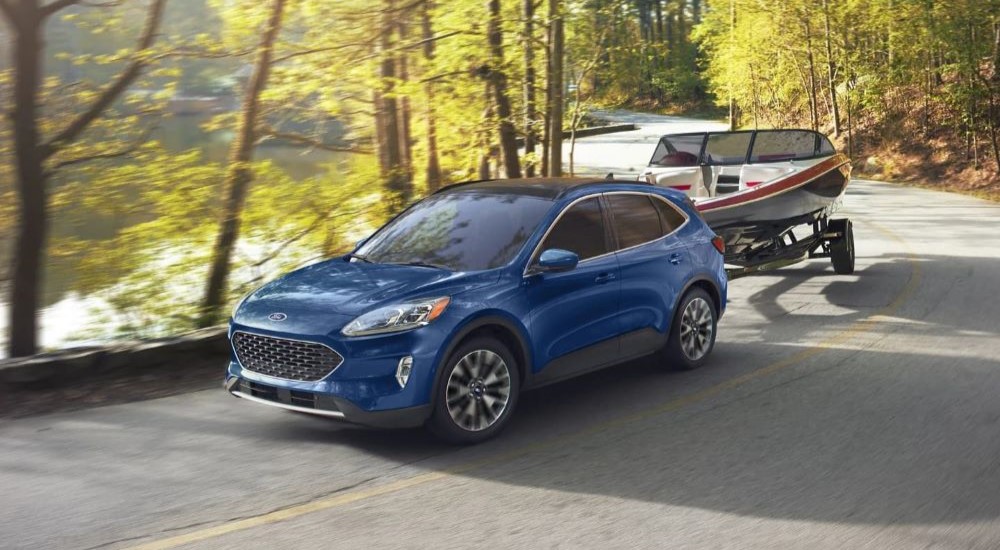 A blue 2022 Ford Escape towing a boat near water.