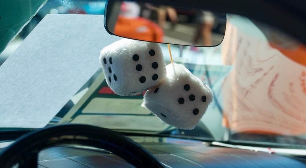 A set of white fuzzy dice dangling in the interior of a vintage car.