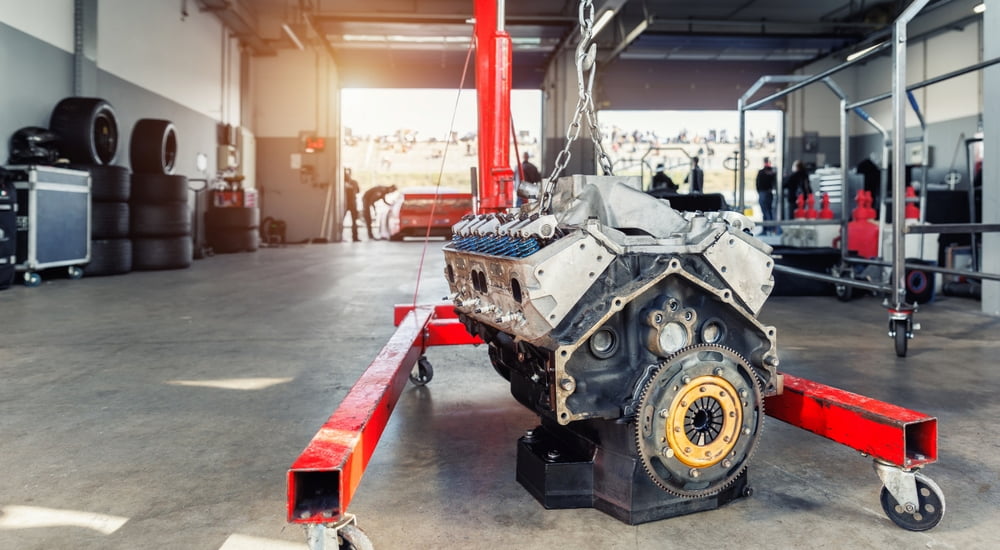 A V8 engine block suspended from a chain in a garage.