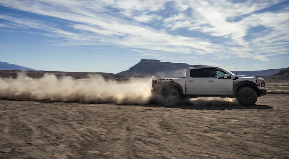 A white 2024 Ford F-150 Raptor is shown driving off-road.