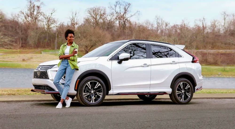 A person leaning against a parked white 2024 Mitsubishi Eclipse Cross.