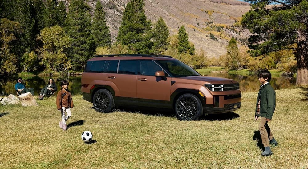 A brown 2025 Hyundai Santa Fe is shown parked near a family.